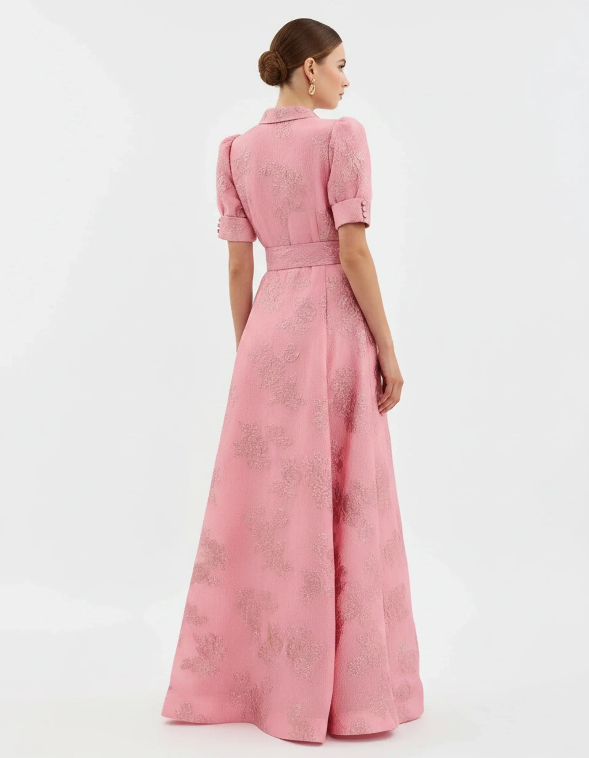Woman wearing a long heavyweight jacquard maxi dress with a textured floral design, short puff sleeves, collared neckline, button-down front, and matching waist belt