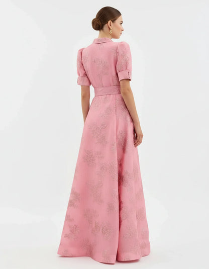 Woman wearing a long heavyweight jacquard maxi dress with a textured floral design, short puff sleeves, collared neckline, button-down front, and matching waist belt