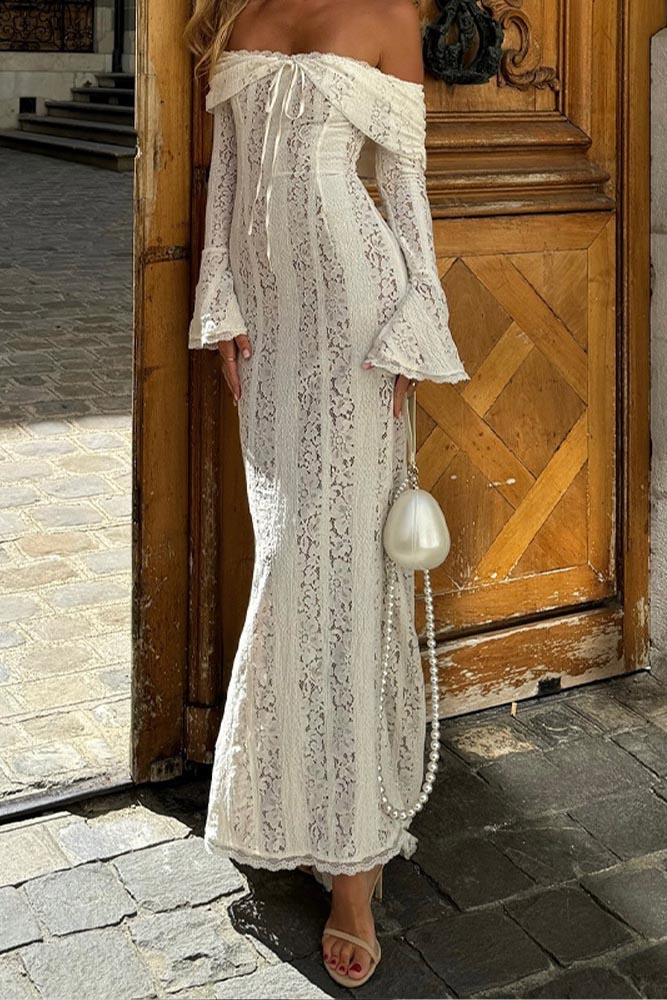 White - A woman wearing an off-white off-the-shoulder lace maxi dress with long flared sleeves and a tie-front detail, standing in front of a rustic wooden door.