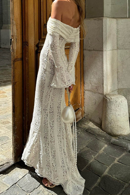 White - A woman wearing an off-white off-the-shoulder lace maxi dress with long flared sleeves and a tie-front detail, standing in front of a rustic wooden door.