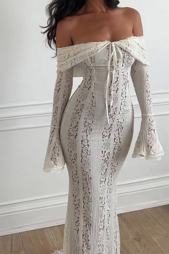 White - A woman wearing an off-white off-the-shoulder lace maxi dress with long flared sleeves and a tie-front detail, standing in front of a rustic wooden door.