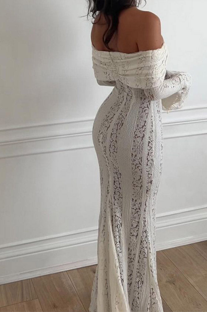 White - A woman wearing an off-white off-the-shoulder lace maxi dress with long flared sleeves and a tie-front detail, standing in front of a rustic wooden door.