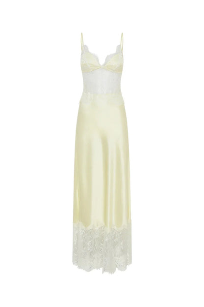 A woman wearing a pale yellow maxi slip dress featuring a sheer floral lace bodice, spaghetti straps, and a lustrous satin skirt finished with a wide scalloped lace hem.