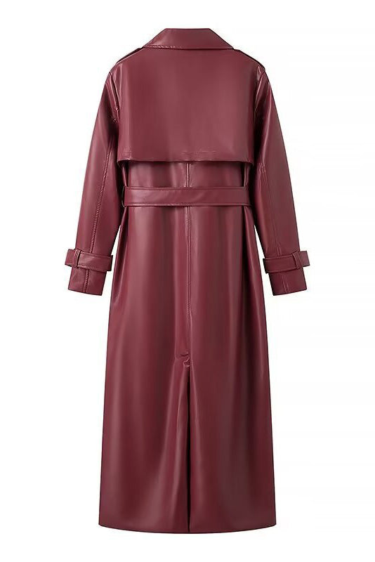 Red - A woman walking down a city street wearing a deep burgundy maxi-length trench coat in a smooth leather-look material, styled with a black turtleneck, black stirrup pants, and black heels.