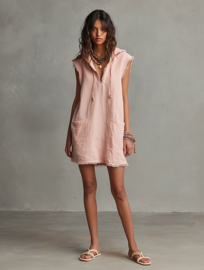 Photo Color - A front view of a model wearing a sleeveless, pale pink textured linen mini dress featuring a hood with drawstrings, frayed edges, front patch pockets, and a relaxed shift silhouette.