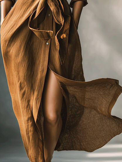 Brown - A woman walking in a long-sleeve, textured brown linen maxi shirt dress with a tied waist, button-up front, and side split, showcasing a fluid drape.
