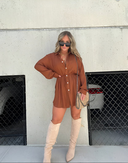 Brown - Woman wearing a long sleeve button front shirt dress with an adjustable tie waist.
