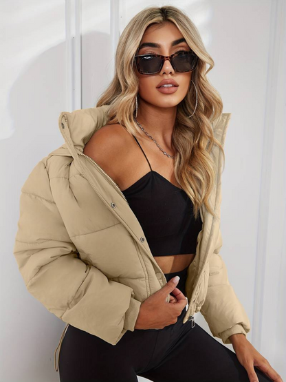 Beige - A woman wearing a chocolate brown cropped puffer jacket with a hood, styled over a black sports bra and high-waisted black leggings.