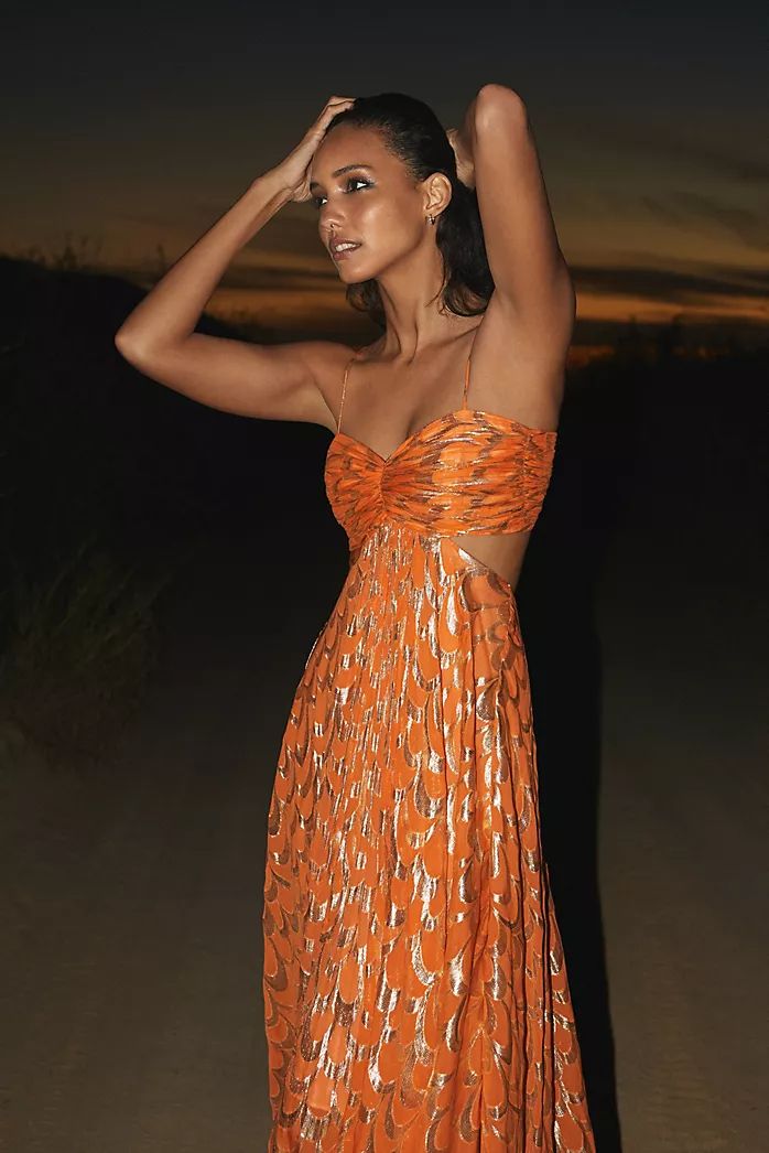 Women's bright orange maxi dress featuring a metallic gold scallop pattern, a ruched sweetheart bodice, side cut-outs, and a voluminous skirt.