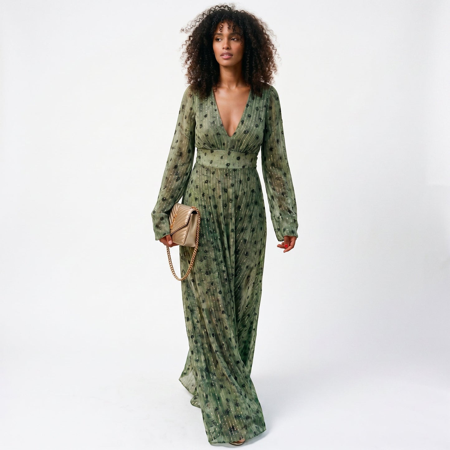 2XL - A woman wearing a long-sleeved, plunging V-neck maxi dress in olive green chiffon with gold metallic vertical stripes and dark abstract spots, holding a gold quilted clutch bag.