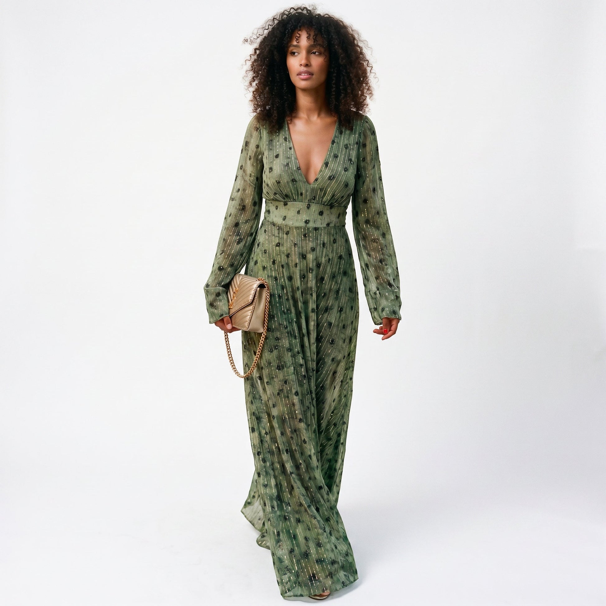 2XL - A woman wearing a long-sleeved, plunging V-neck maxi dress in olive green chiffon with gold metallic vertical stripes and dark abstract spots, holding a gold quilted clutch bag.