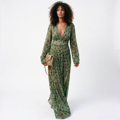 2XL - A woman wearing a long-sleeved, plunging V-neck maxi dress in olive green chiffon with gold metallic vertical stripes and dark abstract spots, holding a gold quilted clutch bag.