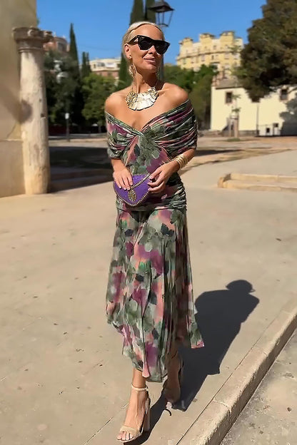 Multi - A woman walking outdoors wearing an elegant off-the-shoulder midi dress featuring a ruched bodice and a vibrant abstract floral print in shades of green, purple, and pink.