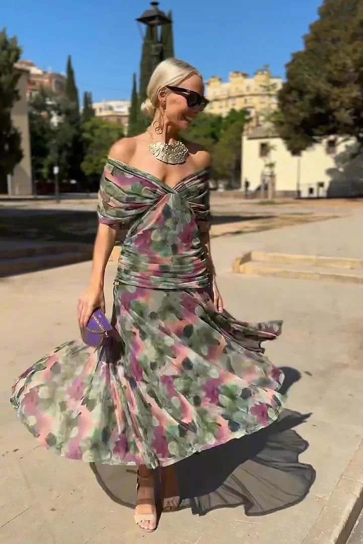 Multi - A woman walking outdoors wearing an elegant off-the-shoulder midi dress featuring a ruched bodice and a vibrant abstract floral print in shades of green, purple, and pink.