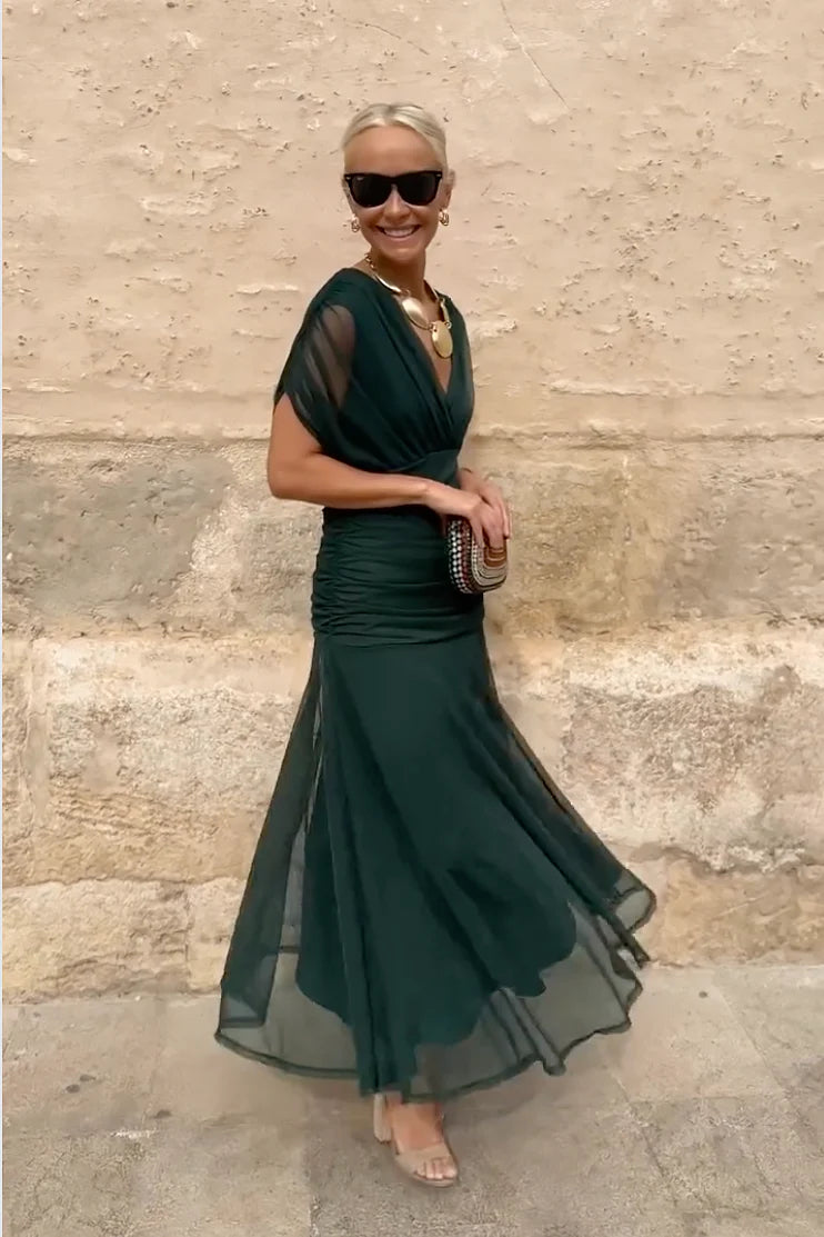 Multi - A woman walking outdoors wearing an elegant off-the-shoulder midi dress featuring a ruched bodice and a vibrant abstract floral print in shades of green, purple, and pink.