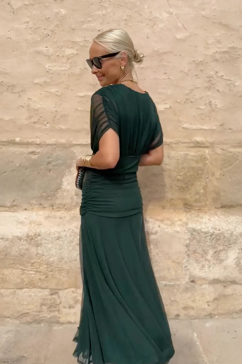Multi - A woman walking outdoors wearing an elegant off-the-shoulder midi dress featuring a ruched bodice and a vibrant abstract floral print in shades of green, purple, and pink.