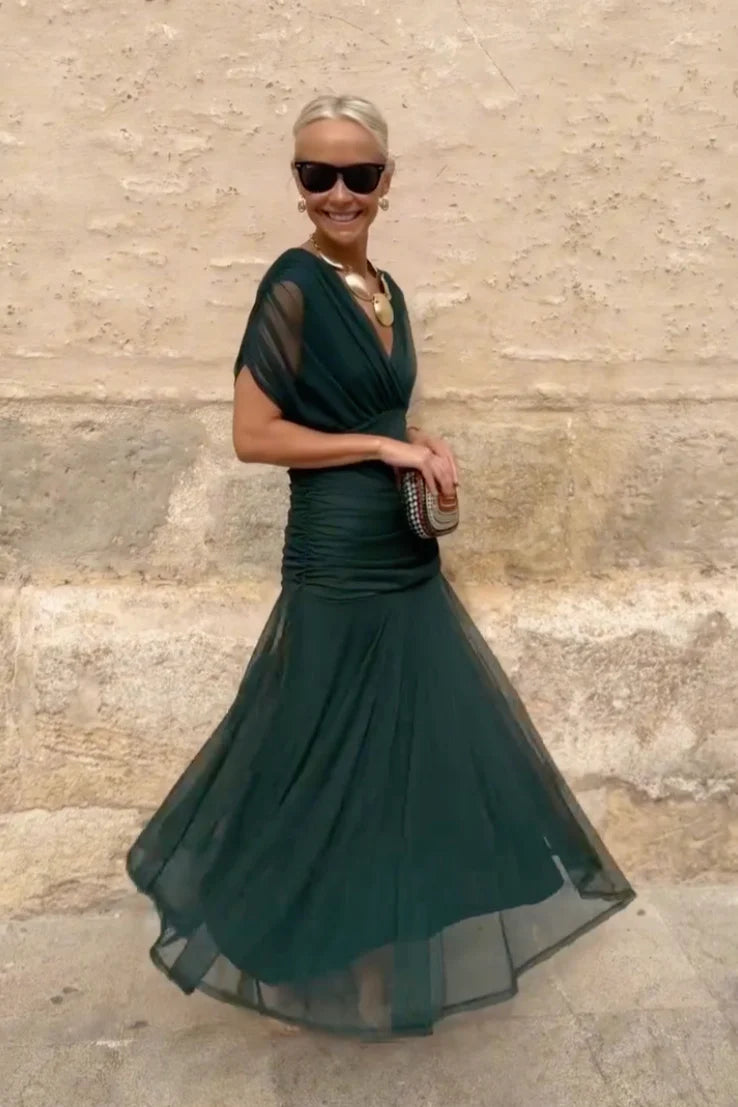 Multi - A woman walking outdoors wearing an elegant off-the-shoulder midi dress featuring a ruched bodice and a vibrant abstract floral print in shades of green, purple, and pink.