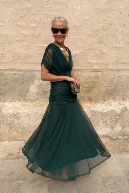 Multi - A woman walking outdoors wearing an elegant off-the-shoulder midi dress featuring a ruched bodice and a vibrant abstract floral print in shades of green, purple, and pink.