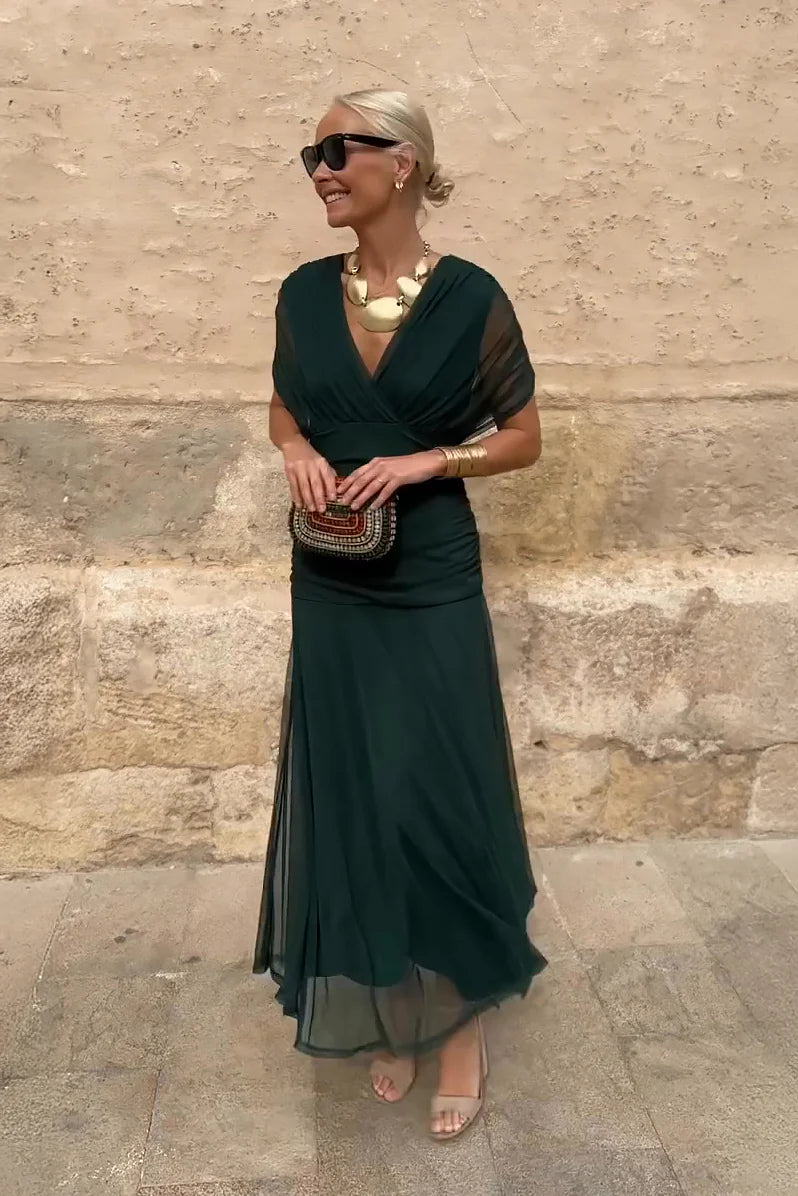 Multi - A woman walking outdoors wearing an elegant off-the-shoulder midi dress featuring a ruched bodice and a vibrant abstract floral print in shades of green, purple, and pink.
