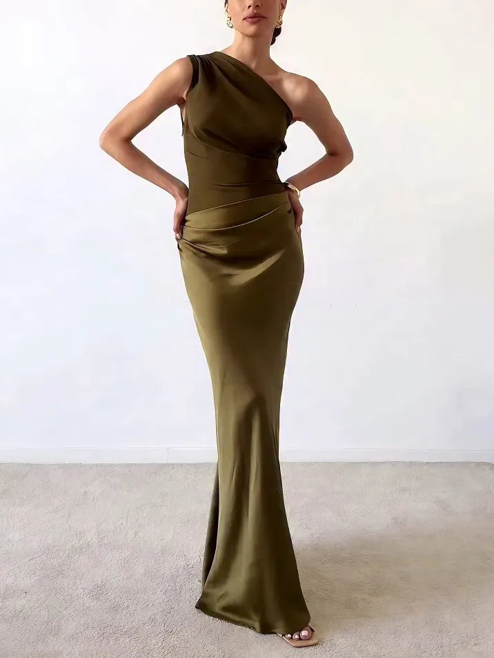 Dark Green - A woman wears a floor-length, one-shoulder maxi dress in a deep chocolate brown. The dress features a matte, draped bodice with an asymmetric waistline that flows into a lustrous, liquid-satin skirt.