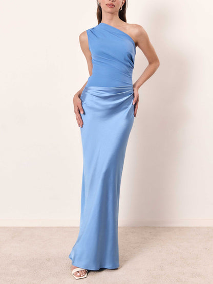 Blue - A woman wears a floor-length, one-shoulder maxi dress in a deep chocolate brown. The dress features a matte, draped bodice with an asymmetric waistline that flows into a lustrous, liquid-satin skirt.