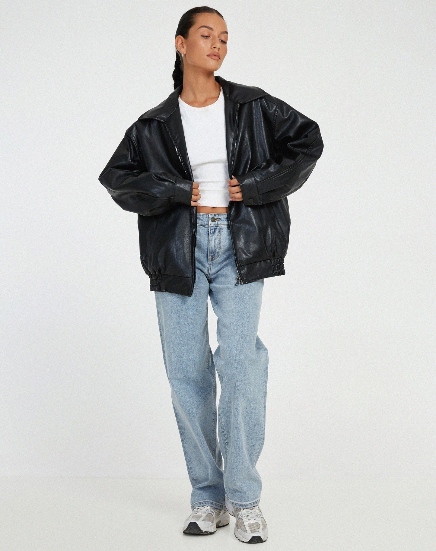 Black - A woman wearing an oversized dark brown faux leather bomber jacket with a wide collar, styled over a black top and plaid mini skirt.