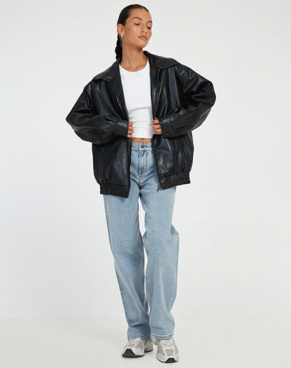 Black - A woman wearing an oversized dark brown faux leather bomber jacket with a wide collar, styled over a black top and plaid mini skirt.