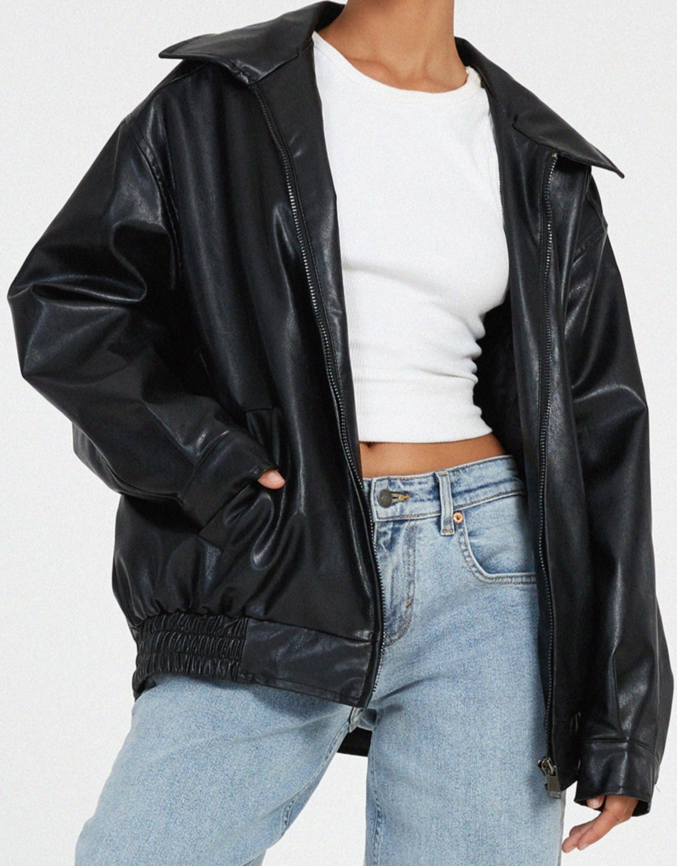 Black - A woman wearing an oversized dark brown faux leather bomber jacket with a wide collar, styled over a black top and plaid mini skirt.