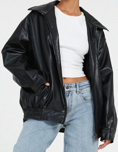 Black - A woman wearing an oversized dark brown faux leather bomber jacket with a wide collar, styled over a black top and plaid mini skirt.