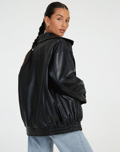 Black - A woman wearing an oversized dark brown faux leather bomber jacket with a wide collar, styled over a black top and plaid mini skirt.