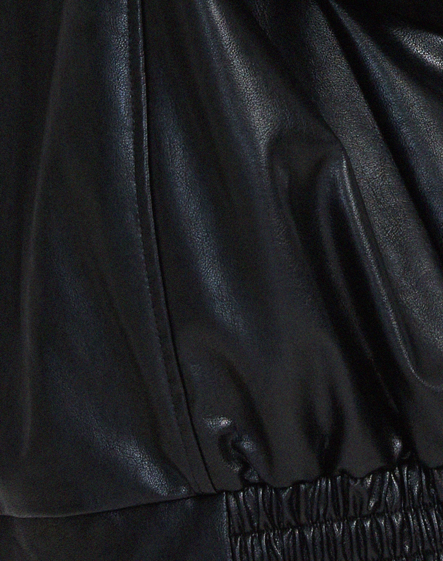 Black - A woman wearing an oversized dark brown faux leather bomber jacket with a wide collar, styled over a black top and plaid mini skirt.