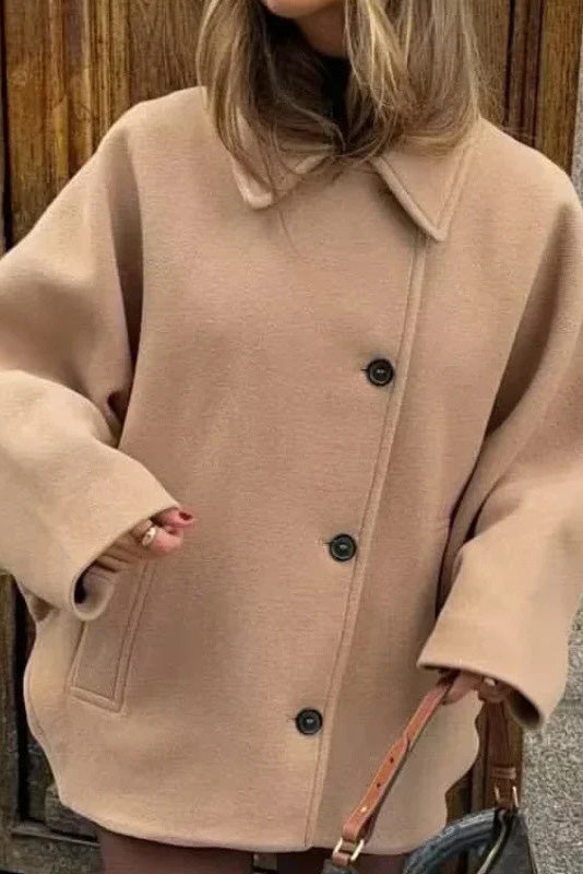 Khaki - A woman wearing a black oversized felted jacket with wide sleeves and notch lapels, styled with a grey turtleneck and black shorts.