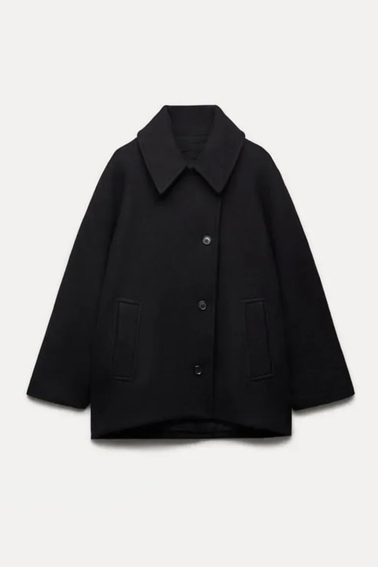 Khaki - A woman wearing a black oversized felted jacket with wide sleeves and notch lapels, styled with a grey turtleneck and black shorts.
