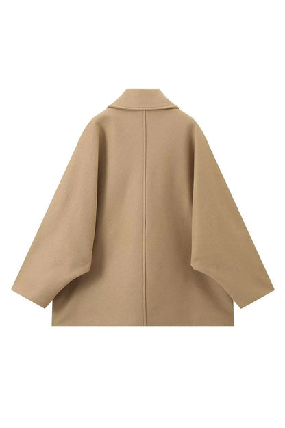 Khaki - A woman wearing a black oversized felted jacket with wide sleeves and notch lapels, styled with a grey turtleneck and black shorts.