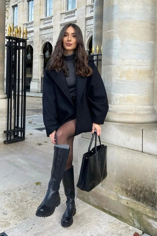 Black - A woman wearing a black oversized felted jacket with wide sleeves and notch lapels, styled with a grey turtleneck and black shorts.