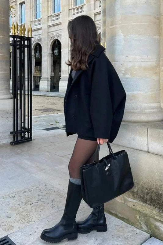 Black - A woman wearing a black oversized felted jacket with wide sleeves and notch lapels, styled with a grey turtleneck and black shorts.