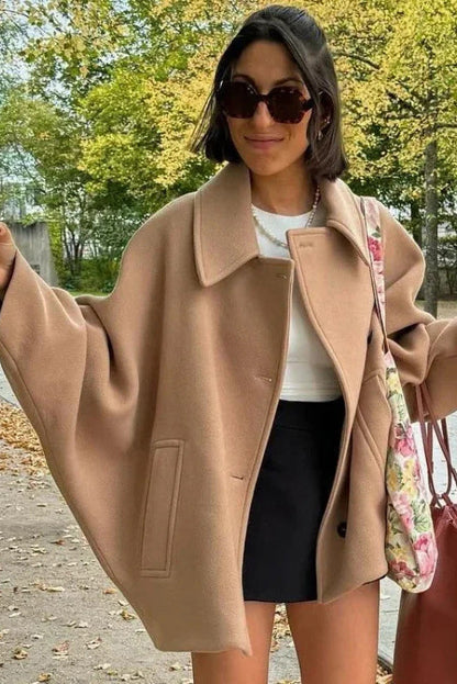 Black - A woman wearing a black oversized felted jacket with wide sleeves and notch lapels, styled with a grey turtleneck and black shorts.