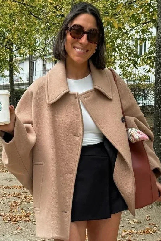 Black - A woman wearing a black oversized felted jacket with wide sleeves and notch lapels, styled with a grey turtleneck and black shorts.