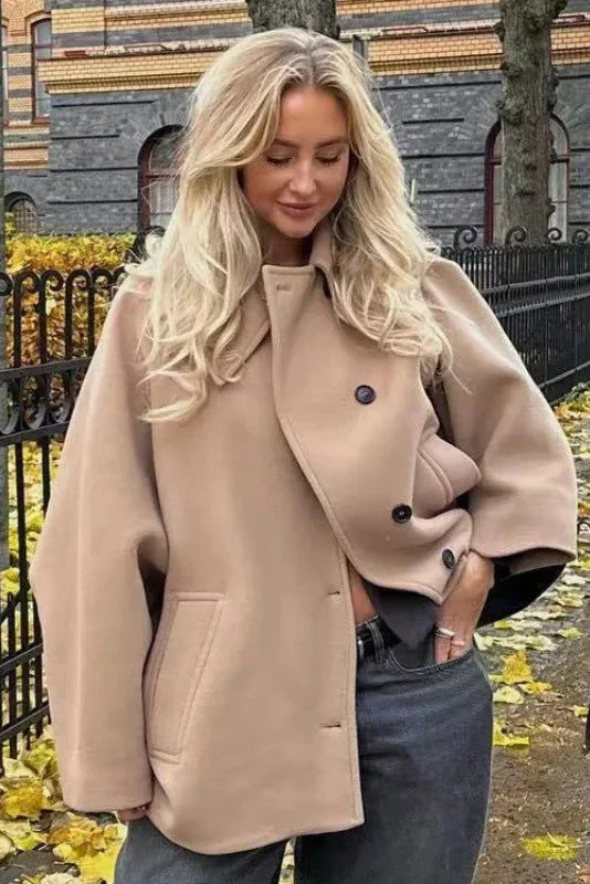 Khaki - A woman wearing a black oversized felted jacket with wide sleeves and notch lapels, styled with a grey turtleneck and black shorts.