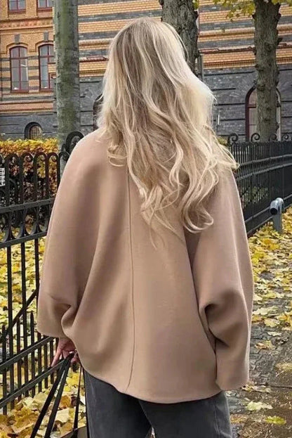 Khaki - A woman wearing a black oversized felted jacket with wide sleeves and notch lapels, styled with a grey turtleneck and black shorts.