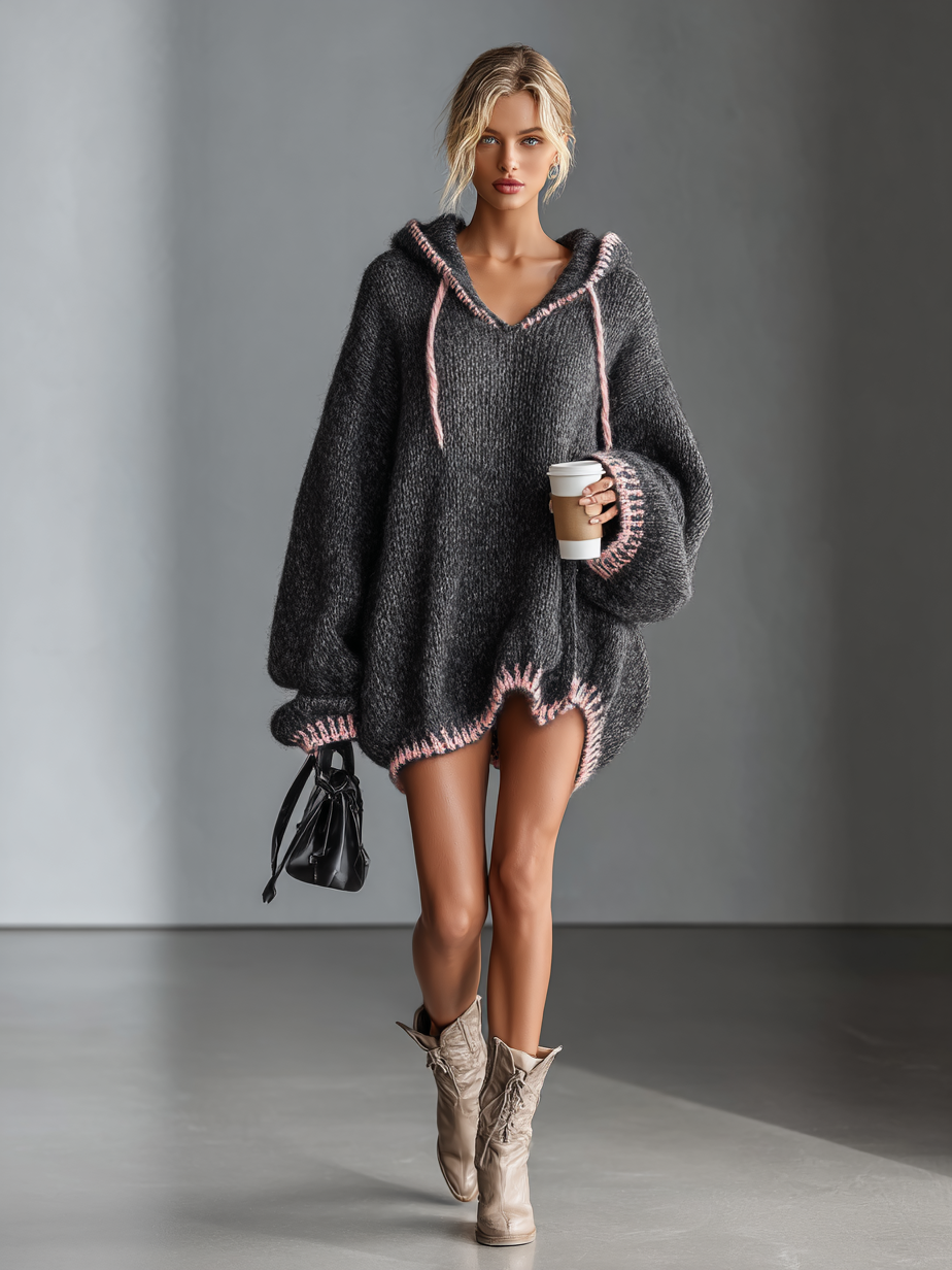 Dark Gray - A woman wearing an oversized charcoal grey textured knit hooded jumper with contrast pink whipstitch detailing on the hood, cuffs, and hem, styled with beige lace-up boots.