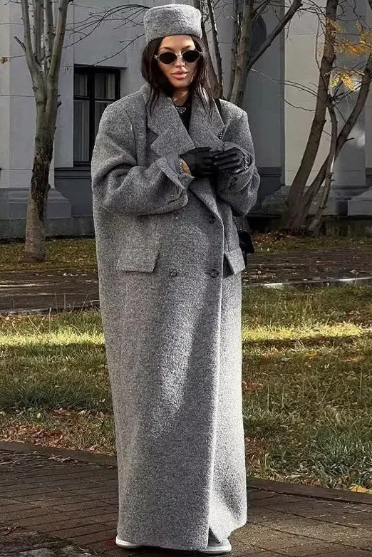 Grey - A woman wearing an oversized, double-breasted maxi coat in textured heather grey wool, featuring wide notched lapels and flap pockets, paired with a matching grey pillbox hat.