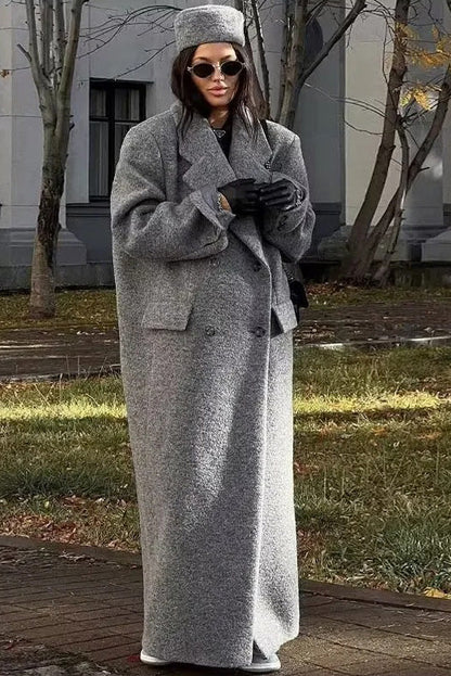 Grey - A woman wearing an oversized, double-breasted maxi coat in textured heather grey wool, featuring wide notched lapels and flap pockets, paired with a matching grey pillbox hat.