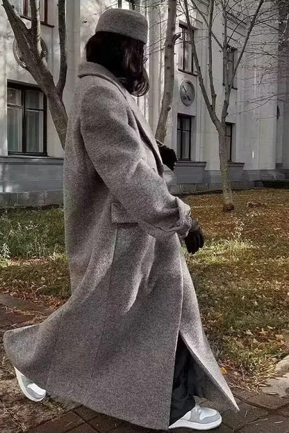 Grey - A woman wearing an oversized, double-breasted maxi coat in textured heather grey wool, featuring wide notched lapels and flap pockets, paired with a matching grey pillbox hat.