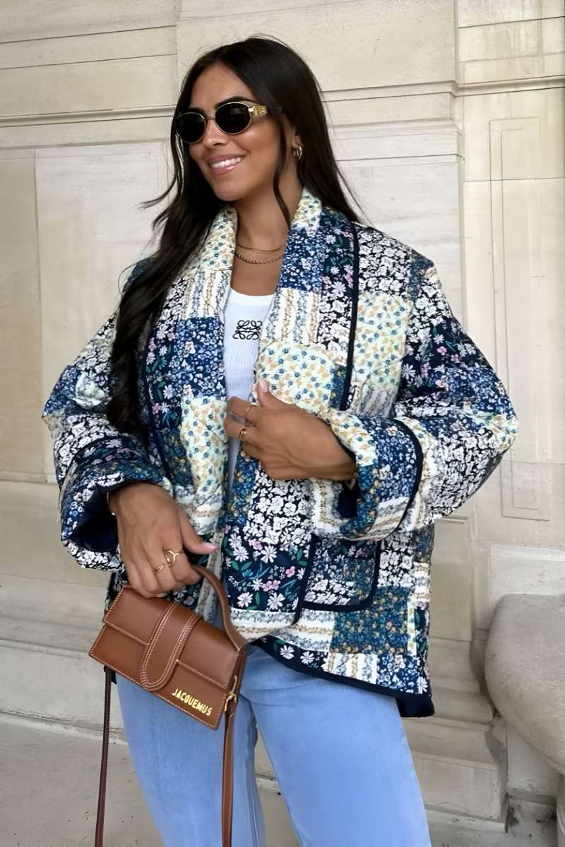 Woman wearing a quilted longline jacket featuring a blue and white floral patchwork design with contrasting dark binding.