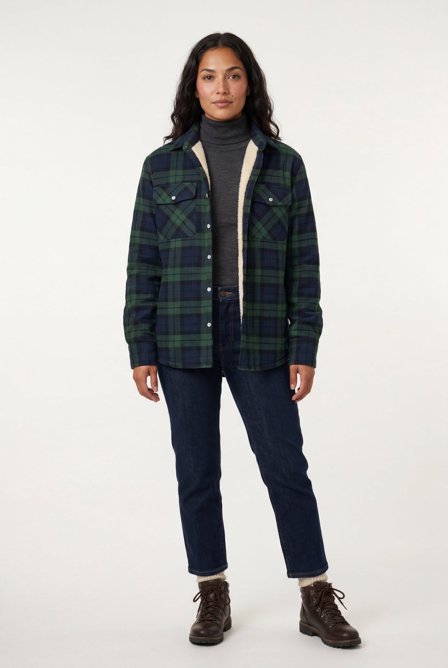 Green - A woman wearing a brown plaid check shirt jacket with a cream-coloured sherpa lining, styled with dark blue slim-fit jeans and brown leather lace-up boots against a plain grey background.
