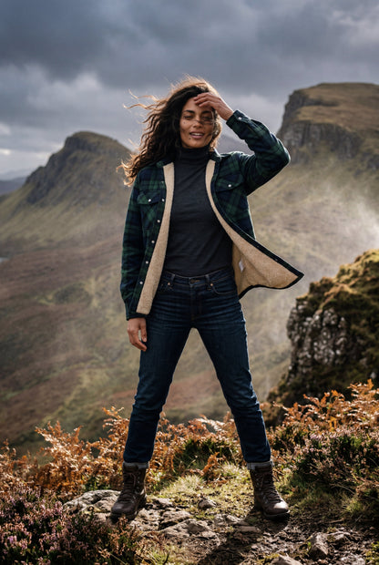 Green - A woman wearing a brown plaid check shirt jacket with a cream-coloured sherpa lining, styled with dark blue slim-fit jeans and brown leather lace-up boots against a plain grey background.