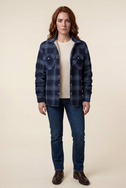 Denim Blue - A woman wearing a brown plaid check shirt jacket with a cream-coloured sherpa lining, styled with dark blue slim-fit jeans and brown leather lace-up boots against a plain grey background.