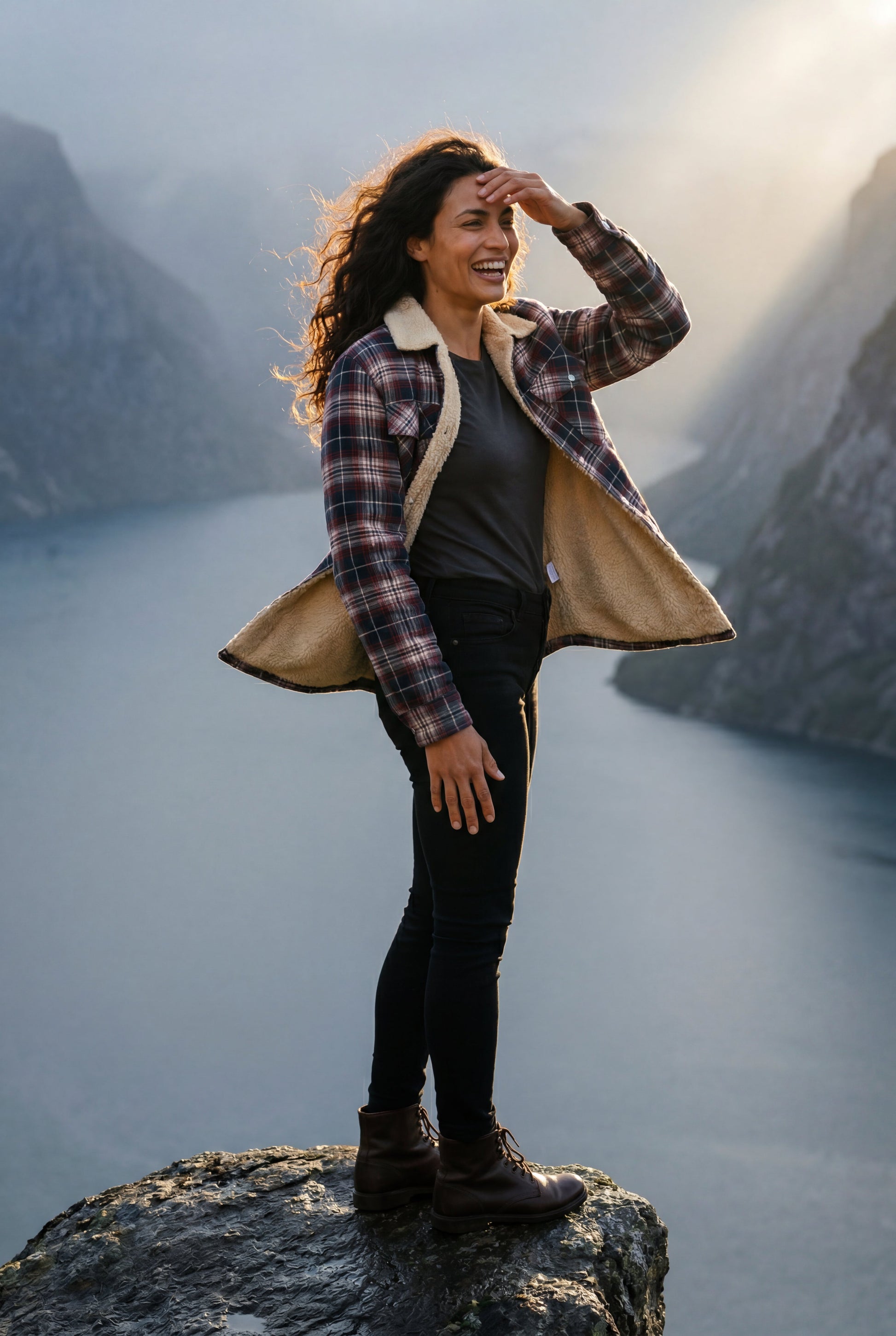 Denim Blue - A woman wearing a brown plaid check shirt jacket with a cream-coloured sherpa lining, styled with dark blue slim-fit jeans and brown leather lace-up boots against a plain grey background.
