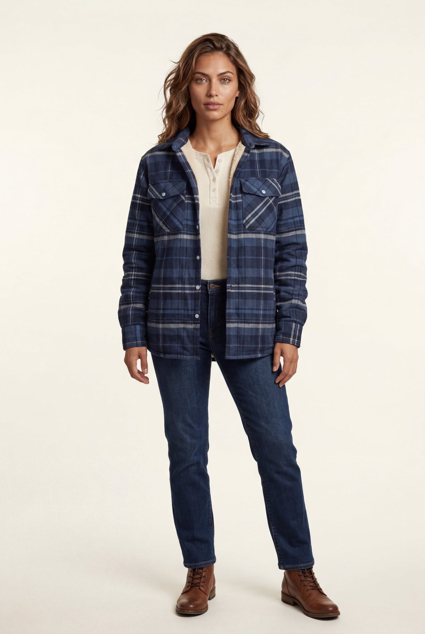 Navy Blue - A woman wearing a brown plaid check shirt jacket with a cream-coloured sherpa lining, styled with dark blue slim-fit jeans and brown leather lace-up boots against a plain grey background.